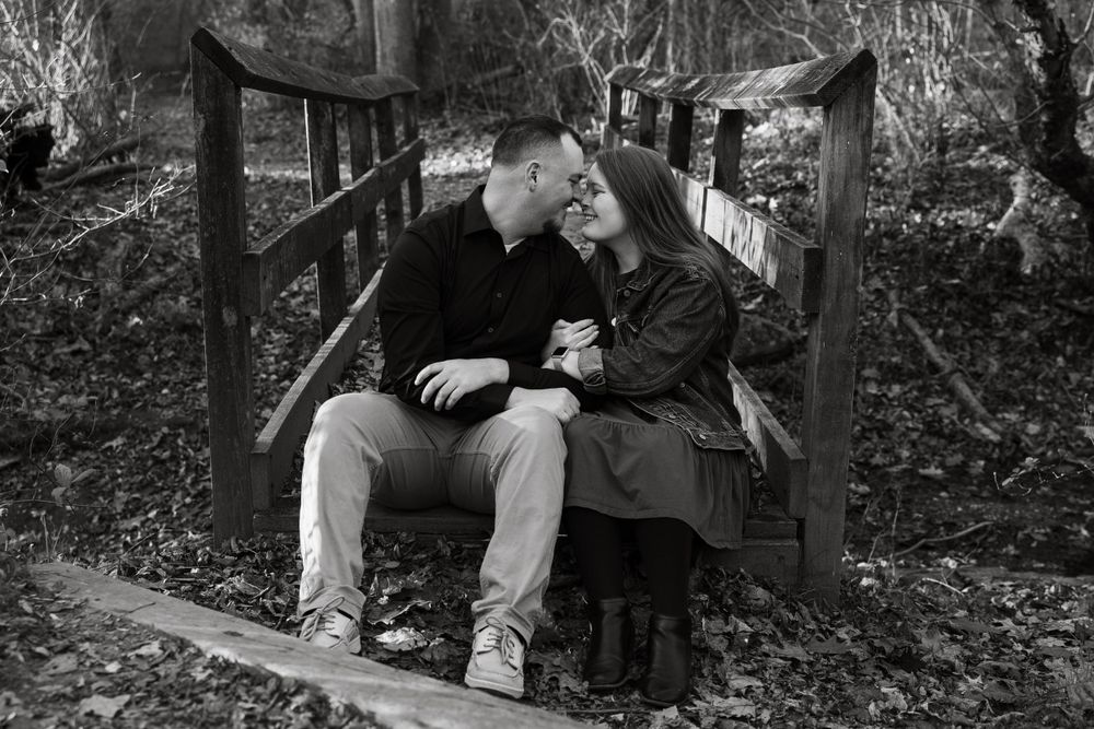 A black and white photo of a couple sitting close together on a wooden bridge.