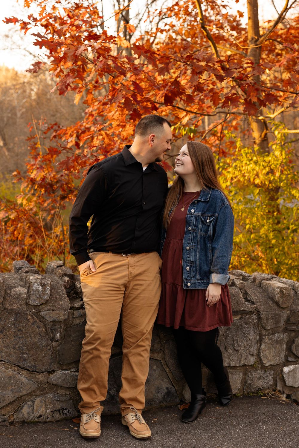 A couple sharing an intimate moment against a stone wall backdrop with vibrant autumn foliage overhead.
