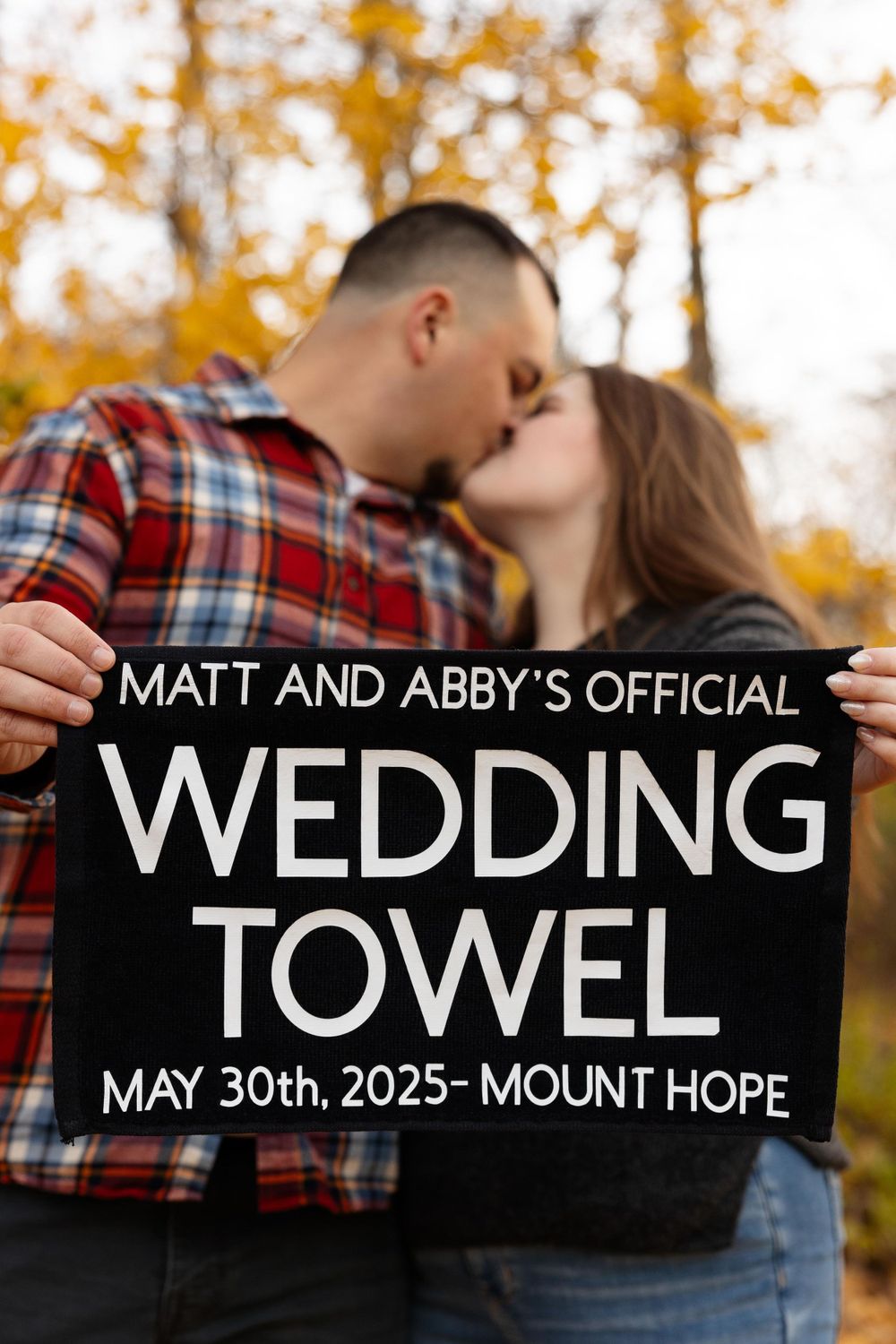A couple kissing while holding a sign announcing their wedding date at Mount Hope in 2025.