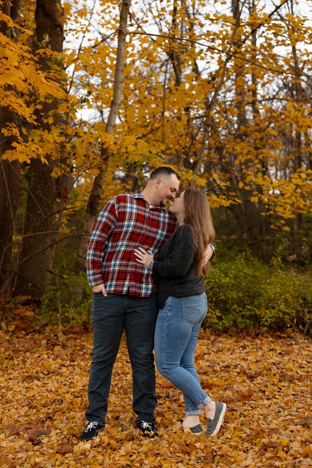 A loving embrace amidst fallen autumn leaves under golden maple trees.