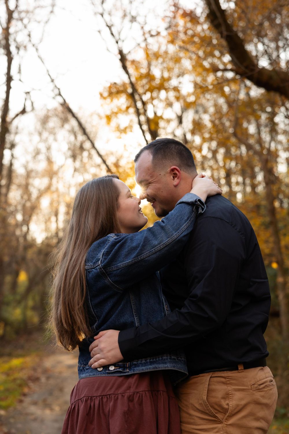 A couple embraces on an autumn path surrounded by golden fall foliage.