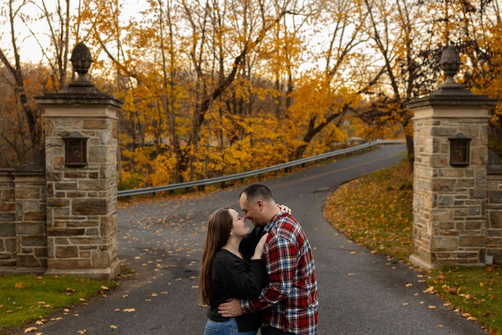A romantic autumn scene at a stone-pillared entrance with golden fall foliage.