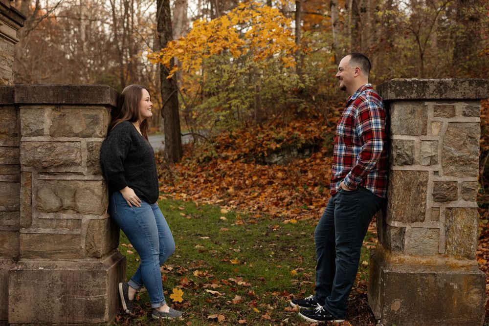 A playful couple posing against stone pillars in a fall setting.