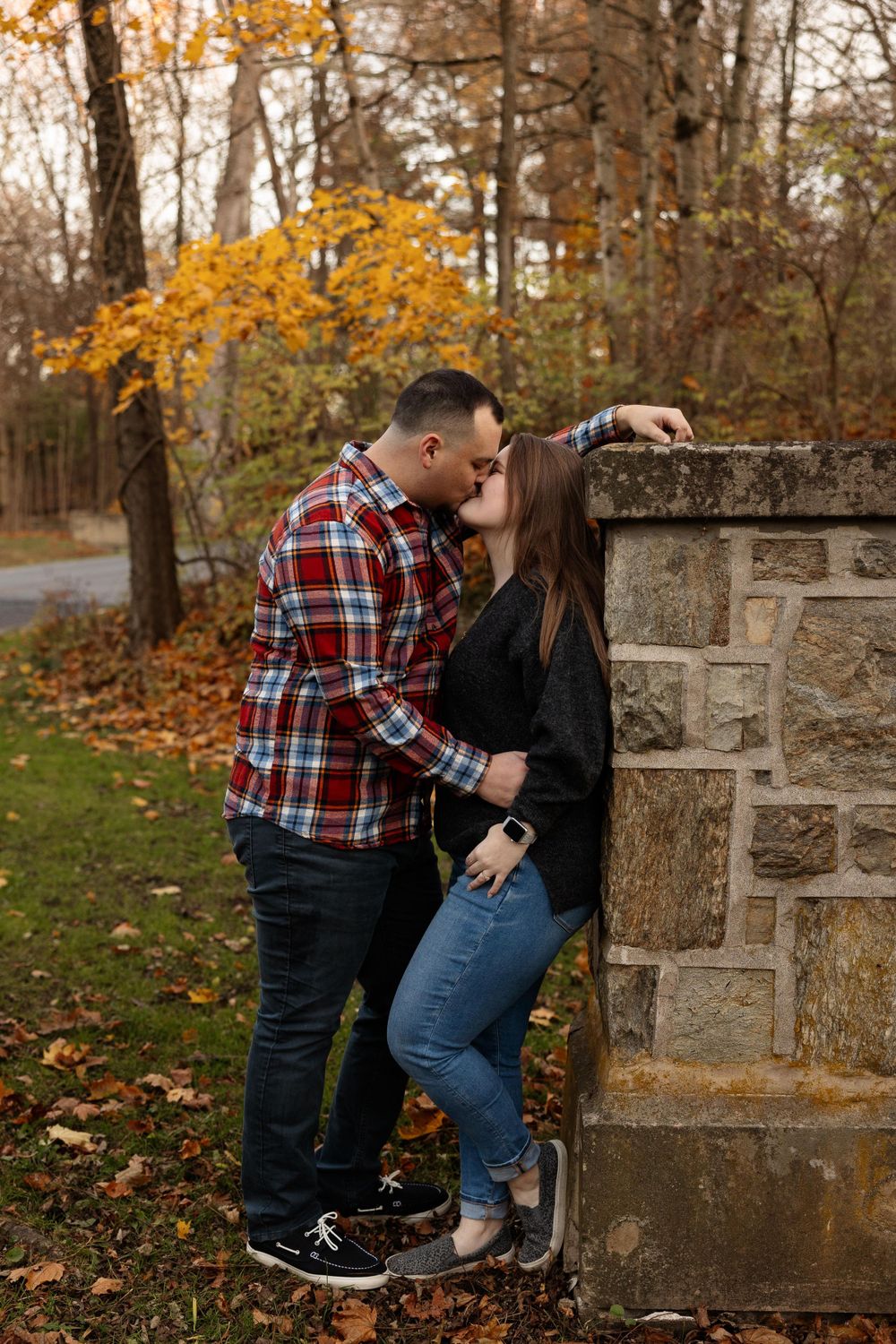 A tender moment shared against a stone pillar surrounded by autumn foliage.