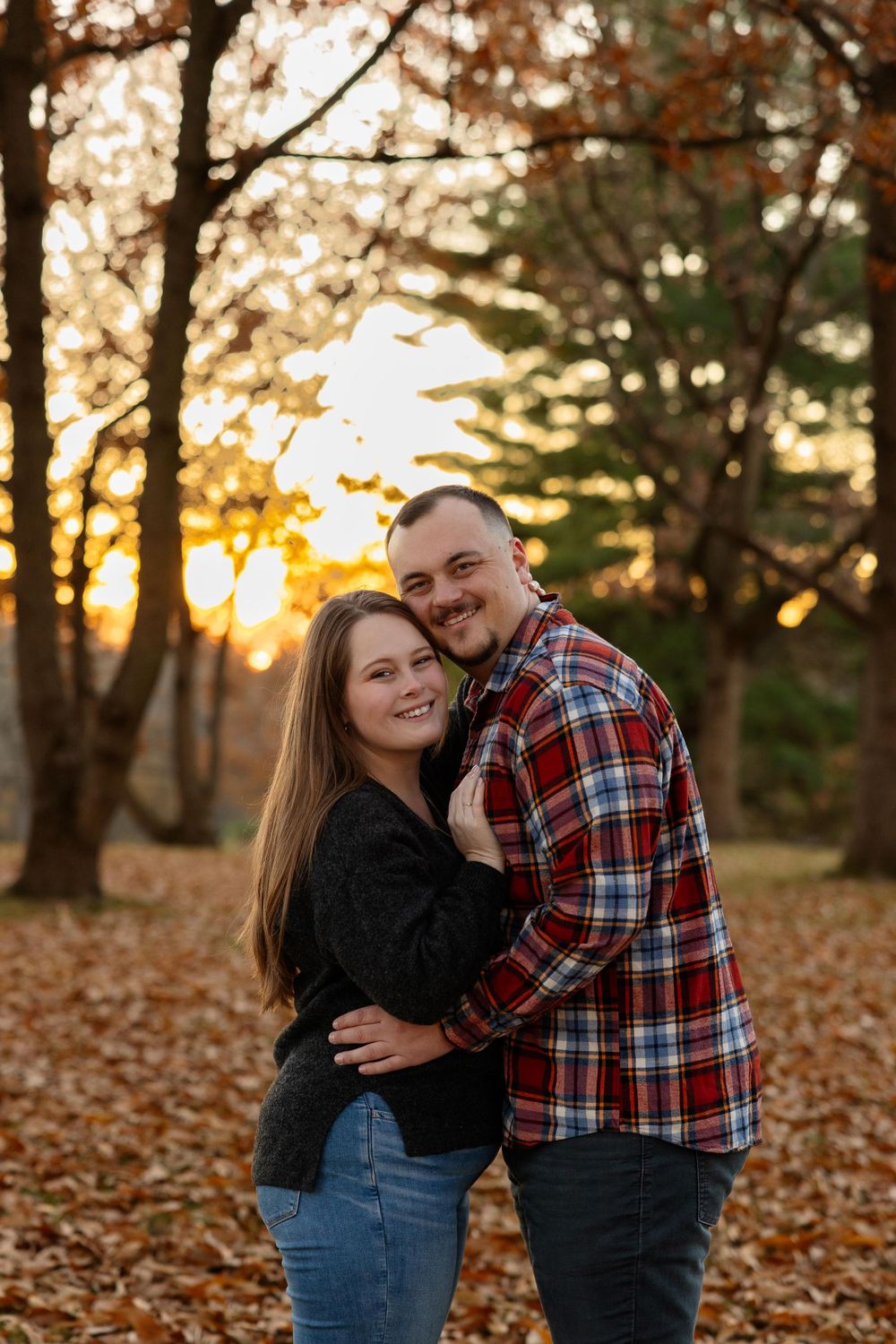A romantic embrace during golden hour with autumn leaves scattered on the ground.