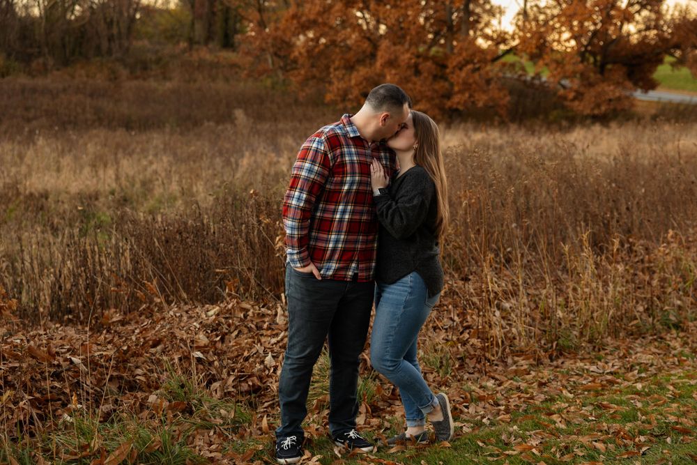 A romantic autumn engagement photo with golden grass and fall foliage in the background.