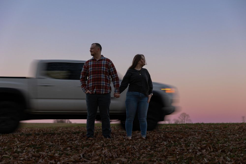 A couple holding hands at twilight with a blurred pickup truck in the background.