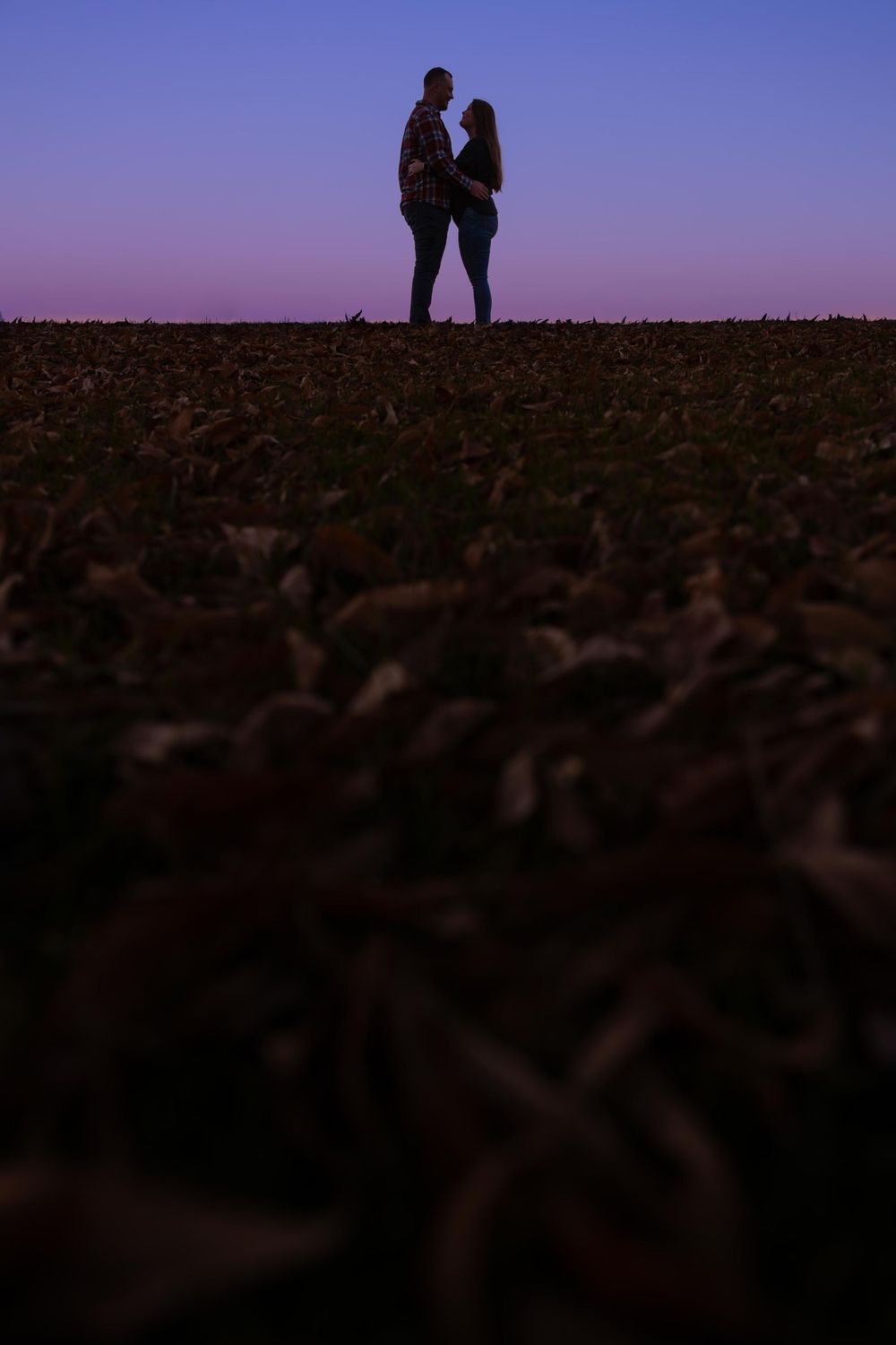 Silhouettes of a couple standing on a hill against a purple sunset sky.