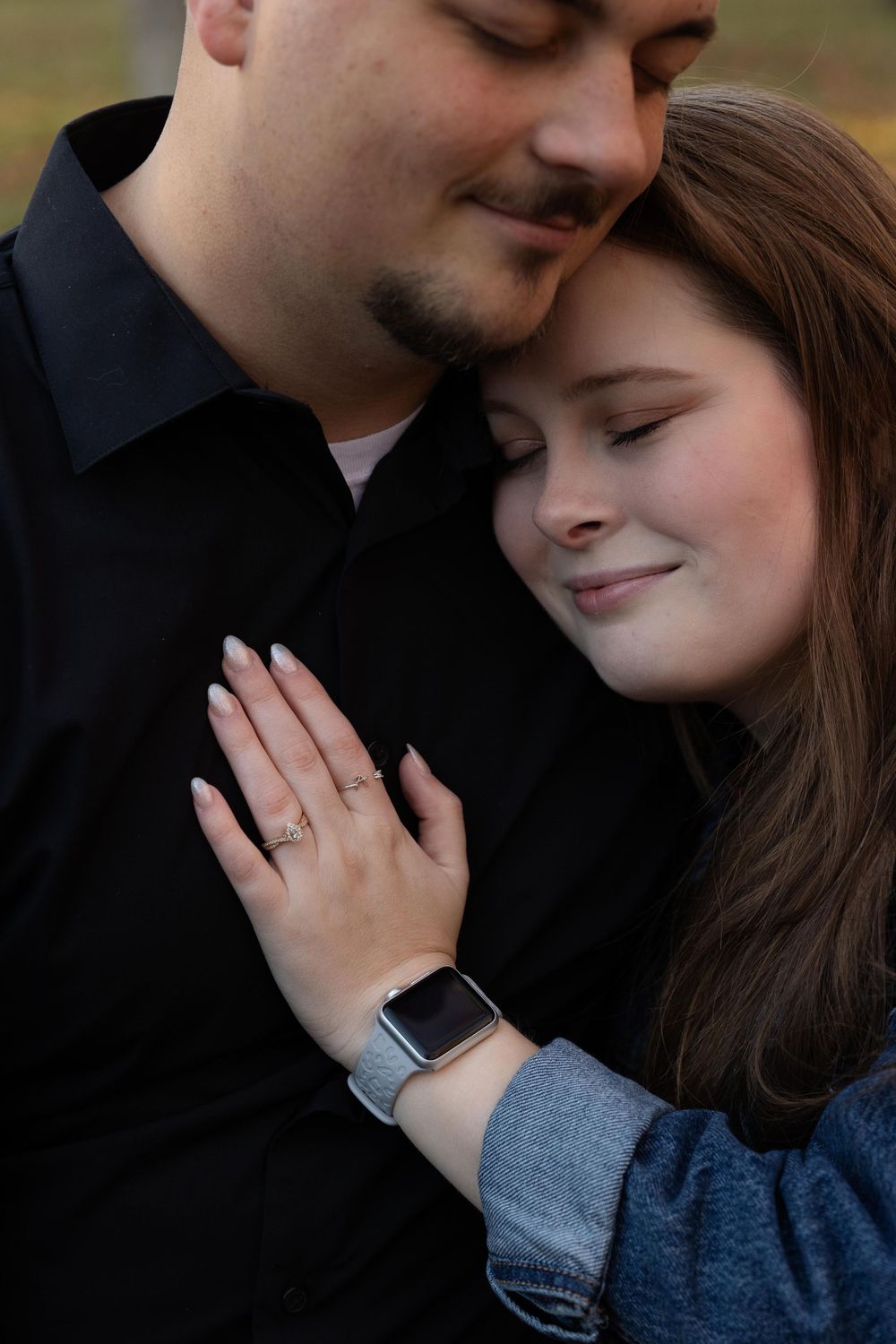 A tender close-up moment between couple with eyes closed showing engagement ring and smart watch.