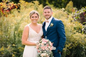 Couple poses with pink and white bouquet against garden backdrop.