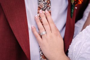 Close-up of engagement ring on hand against burgundy suit jacket.