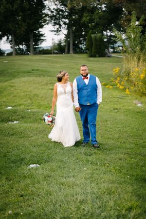 Bride and groom in blue and white stand together on grassy hill during summer wedding.