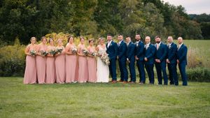 Wedding party lines up on grass with bridesmaids in pink dresses and groomsmen in navy suits.