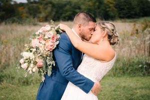 Newlyweds share romantic moment with large pink bouquet during outdoor photoshoot.
