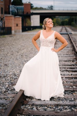 A white wedding dress flows elegantly as bride poses on railroad tracks.
