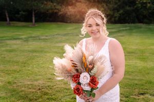 Wedding portrait showing bouquet with pampas grass, roses and dried flowers against green backdrop.