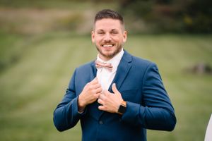 Wedding attire preparation showing a navy suit with pink bowtie against a green landscape.