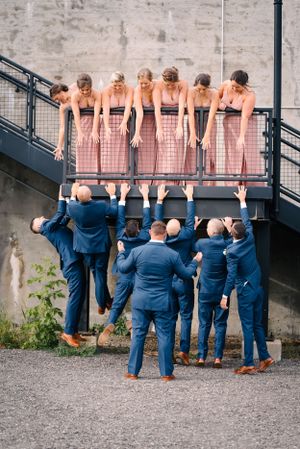 Creative wedding party photo with bridesmaids on balcony and groomsmen looking up from below.