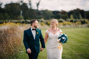 A couple shares a joyful moment while walking through an outdoor field on their wedding day.