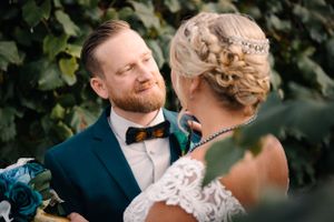Intimate wedding couple moment with groom in navy suit and bride in lace against green vineyard backdrop.