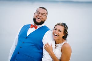 Happy newlyweds share genuine laughter against a cloudy sky backdrop.