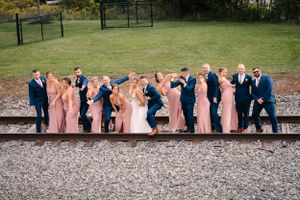 Wedding party poses playfully on railroad tracks with bridesmaids in pink and groomsmen in navy.