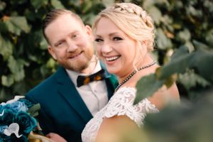 Joyful wedding portrait with couple laughing together against vineyard greenery.