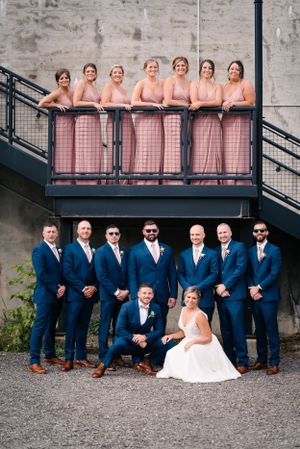 Wedding party poses on industrial staircase with bridesmaids in pink and groomsmen in navy suits.