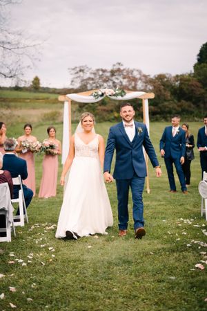 Newlyweds walk down the aisle under a decorated wooden arch with wedding party in background.