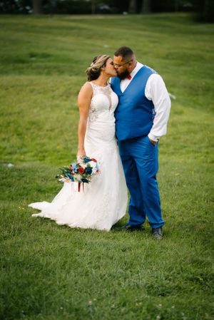 Tender moment between newlyweds on green lawn with bride holding colorful bouquet.