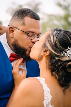 Romantic wedding portrait of a couple sharing a kiss, with the bride in white lace and groom in royal blue.