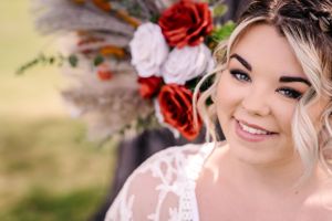 Close-up wedding portrait featuring elegant makeup and a stunning floral bouquet with red roses.