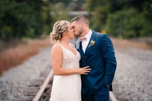 Romantic wedding portrait of a couple sharing a kiss on railroad tracks wearing white dress and navy suit.