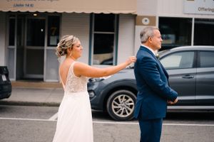 Candid moment between wedding couple in white dress and navy suit outside urban building.