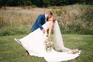 Wedding couple shares romantic dip pose on grassy field with flowing white dress and veil.