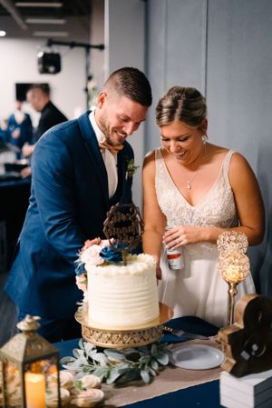Happy couple laughing while cutting their elegant white wedding cake together.