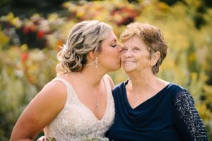 Bride in white lace dress shares tender moment with loved one amid autumn garden.