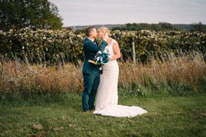 Wedding couple embracing in sunlit field with lace dress and blue bouquet details.