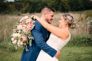Couple embraces during outdoor wedding photoshoot with pink and white floral bouquet.