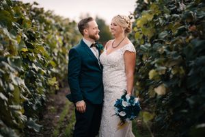 A wedding couple poses intimately between rows of vineyard vines.
