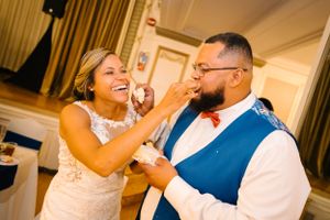 Bride and groom laughing while feeding each other wedding cake during their reception celebration.