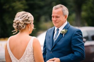 A tender first look moment between a bride in a lace gown and someone in a navy suit at an outdoor wedding.