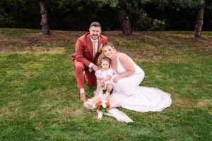 An outdoor family wedding portrait on grass featuring rust-colored formal wear.