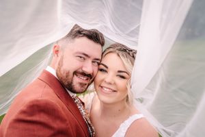 Happy wedding couple shares intimate moment outdoors with flowing veil in background.