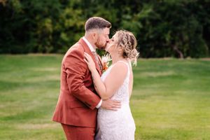 Intimate wedding moment captured outdoors with rust suit and white lace gown.
