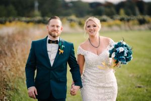 A newlywed couple holds hands while walking through a rustic outdoor setting.