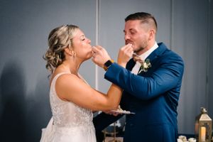 Playful newlyweds feed each other wedding cake in a candid moment.