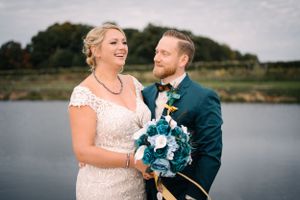 Candid wedding photo shows couple laughing together with lake in background.