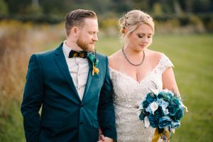 A wedding couple poses together outdoors wearing navy and white formal attire.