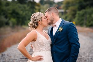 Romantic kiss between newlyweds during outdoor railroad track photoshoot.